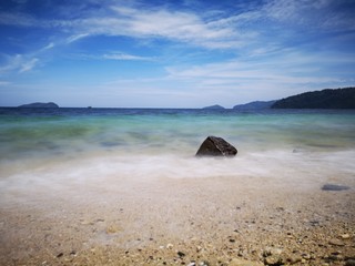 The beautiful silky smooth water waves and rocks on the sea shore during the sunny day.