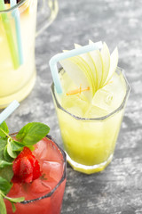 Cold apple ice tea on fray textured background with space for text. Strawberry juice and lemonade pitcher out of focus.