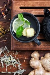 Black cast iron tea pot a cup of hot water with lemon slices and fresh mint with several herbs on brown wooden background flat lay with copy space