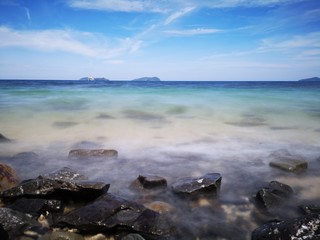 The beautiful silky smooth water waves and rocks on the sea shore during the sunny day.
