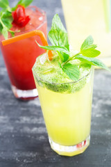 Glass of  fresh cold lemonade on wooden table, lemonade pitcher and strawberry drink out of focus. Copy space available.