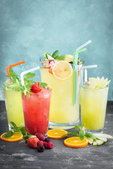 Three glasses of fruit juices and a pitcher full of fresh lemonade on wooden table. Textured background. Copy space available.