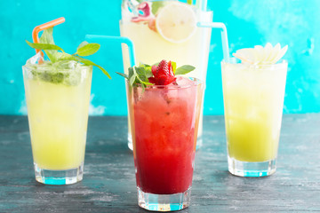 Group of fruit juices with ice and sliced fruits. A jug of lemonade out of focus. Wooden background. Turquoise backdrop. Copy space available.