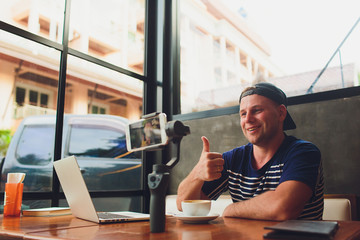 Bearded attractive male video blogger in stylish glasses shoots video streaming for users while...