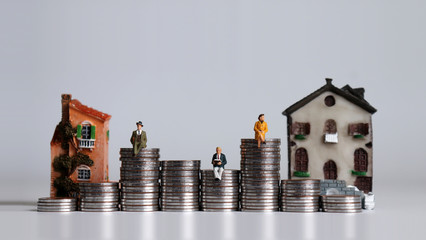 Miniature people and miniature house. Pile of coins in the shape of a graph.