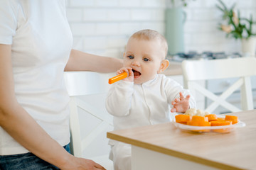 baby eating carrots in the kitchen at the table