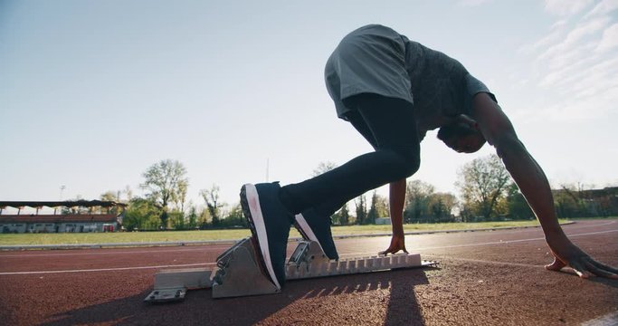 Slow motion of young african male athlete is launching off the start line in a race in athletics stadium.