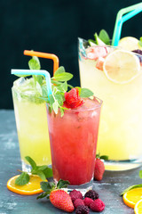 Glass of strawberry drink, lemonade and lemonade pitcher with fruits on black, gray background close up side view