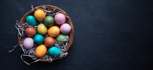 Fototapeta na wymiar Colorful Easter eggs in basket on black wooden background with copy space.