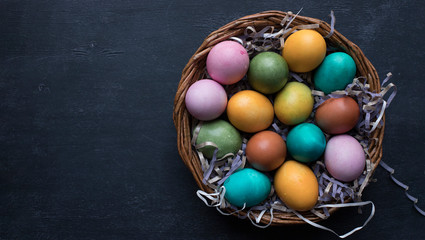 Colorful Easter eggs in basket on black wooden background with copy space.