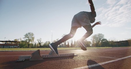 Slow motion of young african male athlete is launching off the start line in a race in athletics stadium. - Powered by Adobe