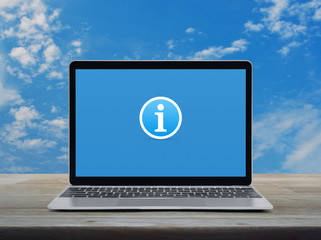 Information sign icon with modern laptop computer on wooden table over blue sky with white clouds, Business customer support online concept