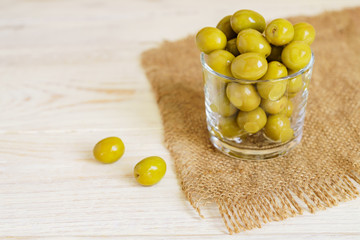 Glass jar of  fresh marinated green olives on burlap cloth on wooden table.