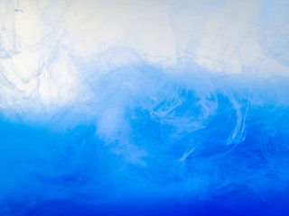 Waves of blue acrylic paint in water, close up view. Abstract background. Acrylic clouds swirling in liquid. Ink dissolving into water, abstract pattern. Drop of paint in liquid. Blurred background