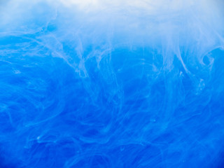 Blue paint in water, close up view. Abstract background. Drop of blue ink dissolved into liquid. Acrylic clouds swirling in water. Waves of acrylic ink, abstract pattern. Blurred background
