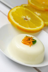Panna cotta with citrus slices on white plate.