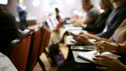 A business conference. Different people sitting by the tables and making marks in the notebook
