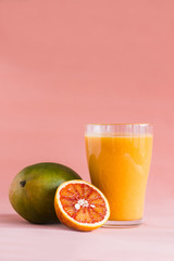 Mango and orange smoothie in glass on pink background.