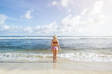 girl in the hat and swimsuit is on the ocean and looks at the water. back view