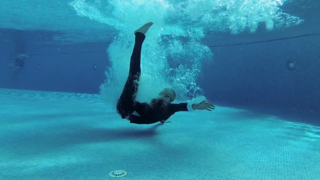 A man in a suit jumps into the pool, tumbles under the water and floats to the surface in a cloud of bubbles. Slow motion. Underwater photography. 4K. 25 fps