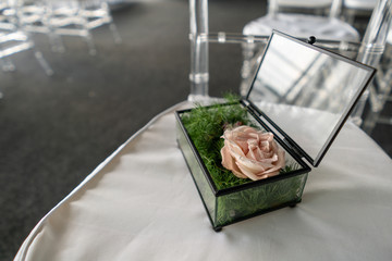 Glass box with pink rose and greenery for wedding rings. Blurred background with wedding . Event decoration with fresh flowers.