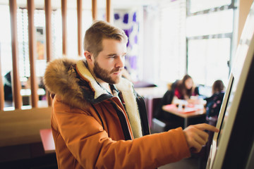 A man orders food in the touch screen terminal with electronic menu in fast food restaurant.