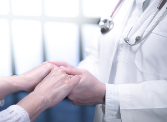 Medical doctor reassuring patient by holding patient’s hands in hospital setting