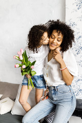 Mom and little cute curly girl spend time together, hugging and kissing each other