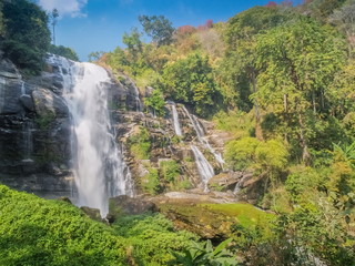 Obraz premium Wachirathan Waterfalls, beautiful waterfall flowing from high cliff around with green forest and blue sky background, Doi Inthanon National Park, Chiang Mai, northern Thailand.