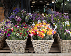 Fototapeta na wymiar Everyday flowers counter with variety of fresh cut flowers such as anemone coronaria, persian buttercups, freesia, statice salem, syringa branches for home decor at the greek garden shop.