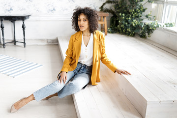 A young, pretty woman with curly hair, dressed in a jacket and jeans, sitting on the steps