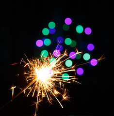 Bengal fire sparkles on the background of Christmas lights on black background. Bewitching dance of sparks.