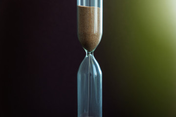 Hourglass in the center. Sand strews down on a brown background. Time flow.