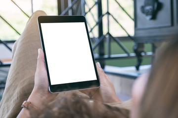Mockup image of a woman holding black tablet pc with blank white desktop screen while laying down in living room with feeling relaxed