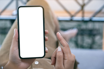Mockup image of a woman holding black mobile phone with blank white desktop screen while laying down in living room with feeling relaxed