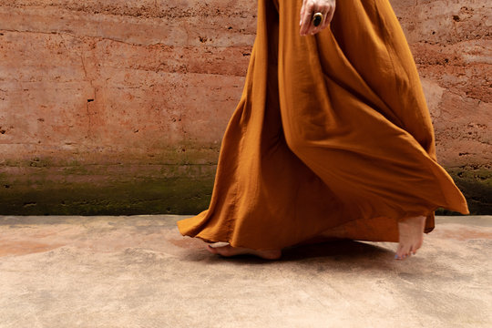 Unrecognisable cropped barefooted woman in a dress walking by the rammed earth wall.
