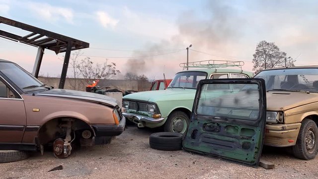 Old broken cars in a landfill. Abandoned, a fire burns in a barrel.Fast motion. Time lapse.