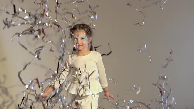 Slow motion of kid jumping and throwing up silver tinsel.