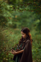 Girl in a cape with a basket walking in a forest