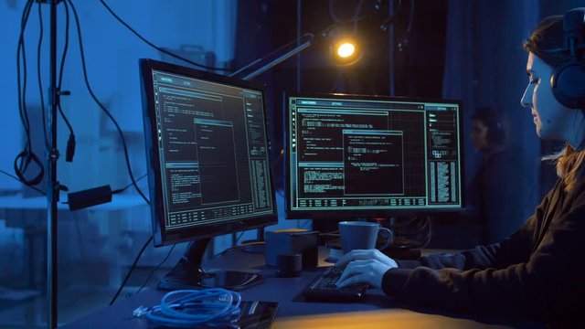 cybercrime, hacking and technology concept - female hacker in dark room creating code or using computer virus program for cyber attack