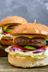 Burgers with juicy cutlet, fresh vegetables, crispy bun with sesame seeds on a wooden table. Close-up. Traditional fast food.