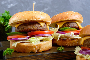 Burgers with juicy cutlet, fresh vegetables, crispy bun with sesame seeds on a wooden table. Close-up. Traditional fast food.