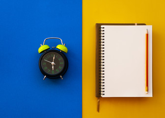 Blank white notepad with pencil and alarm clock isolated on two tone yellow and blue background. - 260956542