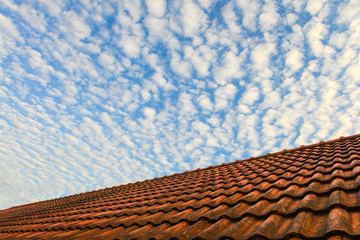 Red house roof and blue sky with white fluffy clouds