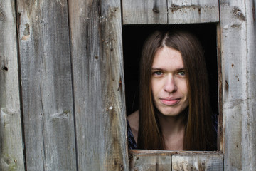 Young long-haired woman looks out of the wooden shed windows.