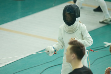A girl fencer having fencing duel on tournament. Wearing a costume and a helmet