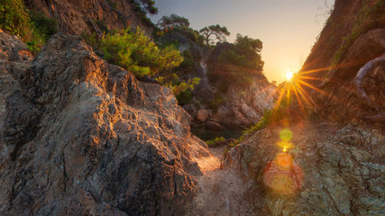 Scenery spanish rocky coast at sunrise. Sun shines from rocks on sea bay in Costa Brava