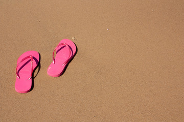 Fototapeta na wymiar pink flip-flops on yellow sand at the water's edge on the beach