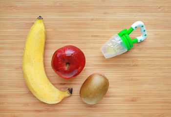 Baby's nibbler and fresh ripe fruits (apple, banana and kiwi) on wood background. Organic baby food concept.