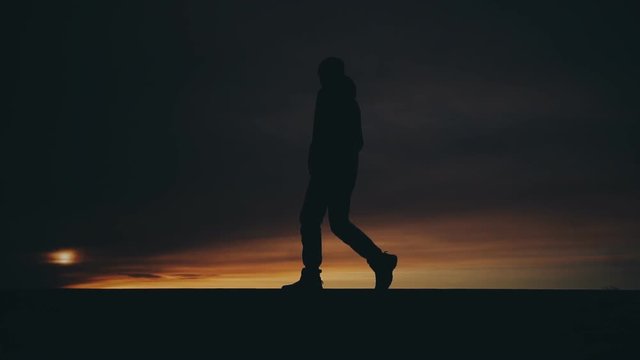 lonely man walking alone on the horizon line at sunset